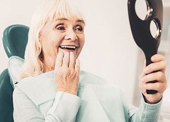 A woman admiring her dentures in a hand mirror