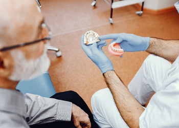 A dentist explains to an older male patient how dental implant supported dentures work and whether he is a qualified candidate