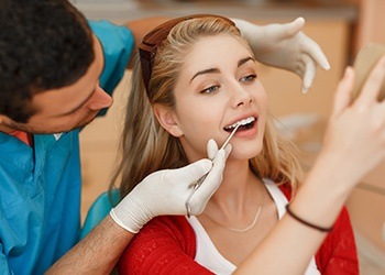 Woman looking at smile in mirror after porcelain veneer cosmetic dentistry treatment