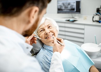 elderly woman smiling at her dentist during advanced dental implant procedure visit