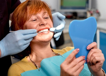 An older woman with red hair admires her smile in the mirror after receiving dentures in Crown Point