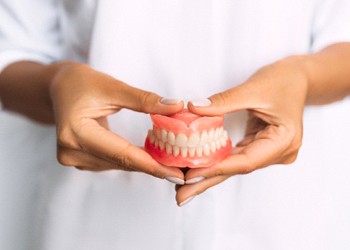 An up-close view of a dental professional holding a full set of dentures in-between their hands