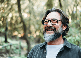 a man with dentures smiling while in the woods