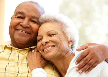 An older couple hugging and smiling while seated on a couch