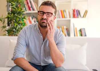 man with failed dental implants sitting on a couch and holding his cheek in pain