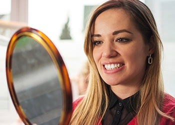 Woman looking at smile in mirror after metal free dental restorations