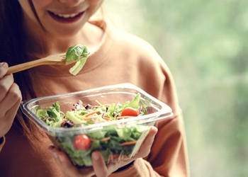A woman eating a salad full of leafy greens and vegetables