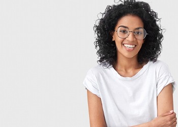 A woman wearing a white t-shirt and glasses and smiling after receiving positive feedback from her dentist