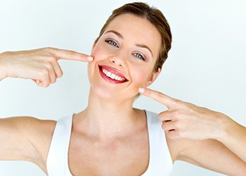 Woman pointing to smile after learning more about the cost of veneers in Crown Point