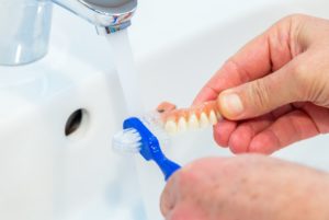 Person cleaning their dentures in a sink