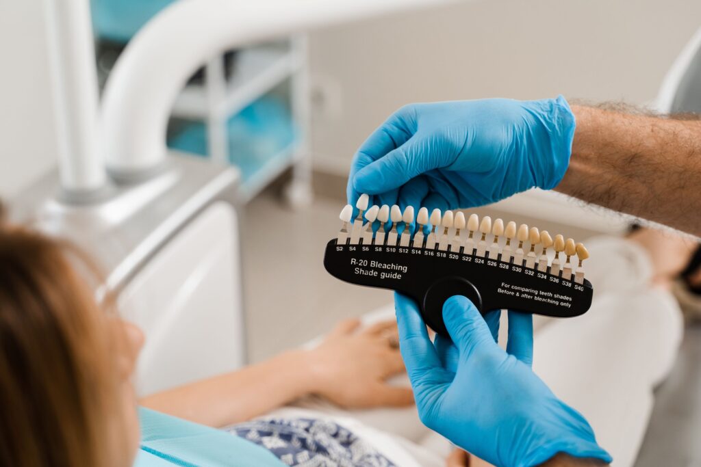 Dentist wearing blue gloves holding shade guide close to patient