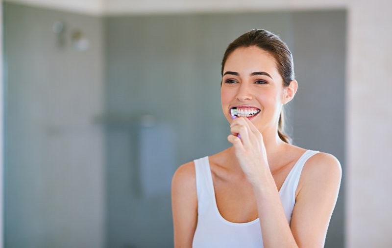 A woman practicing oral hygiene in front of a bathroom mirror